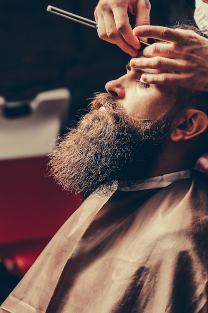 Bearded man with long beard getting hair shaving with razor