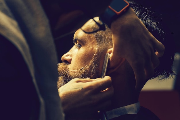 Uomo barbuto con la barba lunga che si fa la barba con il rasoio