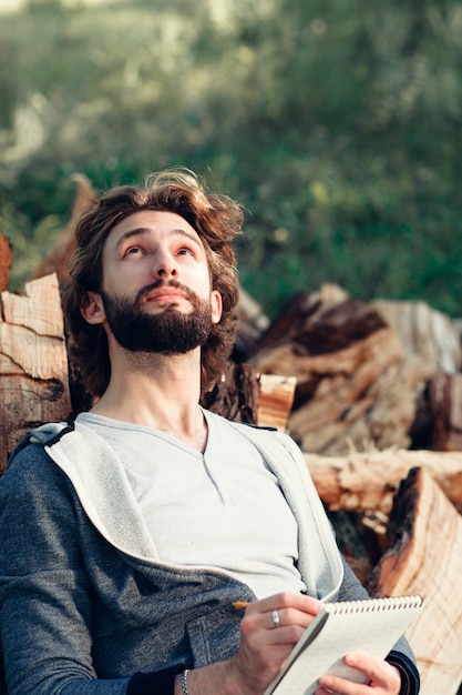 Bearded man with notebook on pile of wood.