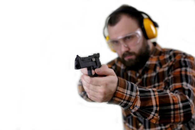 Foto uomo barbuto con occhiali protettivi e addestramento all'orecchio nel tiro con la pistola