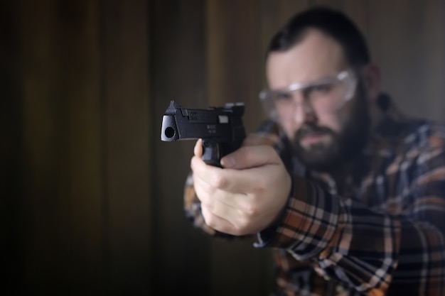 Bearded man with put on protective goggles and ear training in pistol shooting