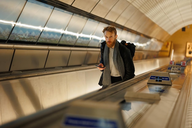 Uomo barbuto con uno smartphone su una scala mobile nella metropolitana