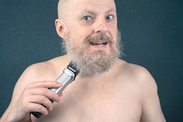 Uomo barbuto con rifinitore per aggiustare la barba in mano. toelettatura e barbiere stile alla moda. correzione della lunghezza della barba