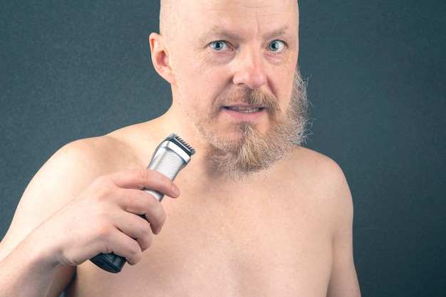 Bearded man with trimmer to adjust beard in hand. grooming and fashionable style barbershop. Beard length correction