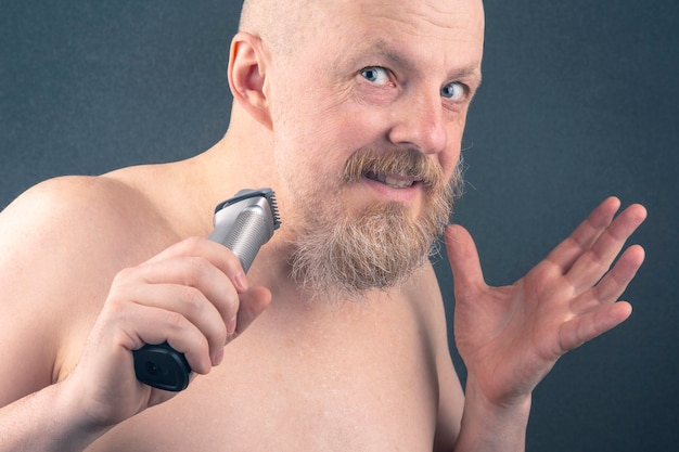 Photo bearded man with trimmer to adjust beard in hand. grooming and fashionable style barbershop.