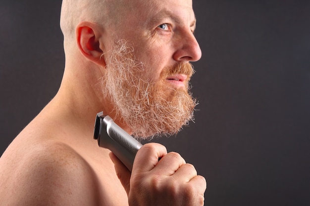 Bearded man with trimmer to adjust beard in hand