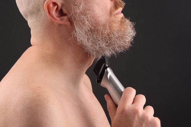 Bearded man with trimmer to adjust beard in hand