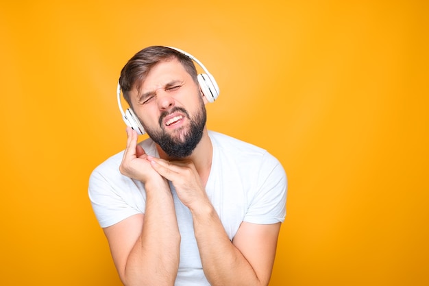 Бородатый мужчина в белых музыкальных наушниках одновременно слушает музыку и поет.
