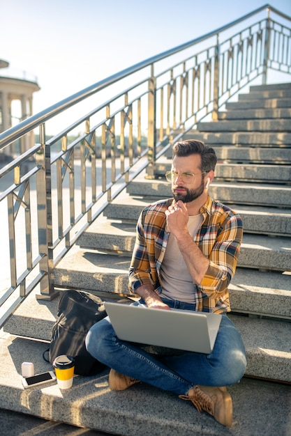 Bearded man working on a laptop on the stairs