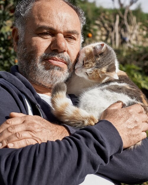 Foto uomo maturo barbuto felice che tiene e abbraccia il suo gatto carino amicizia amore amore degli animali