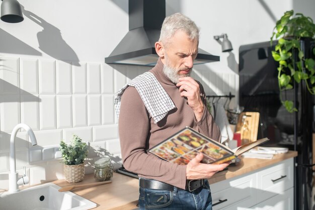 Foto uomo maturo barbuto che cerca una ricetta in un libro di cucina