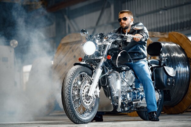 Bearded motorcyclist in black leather clothing with his motorbike on underground parking