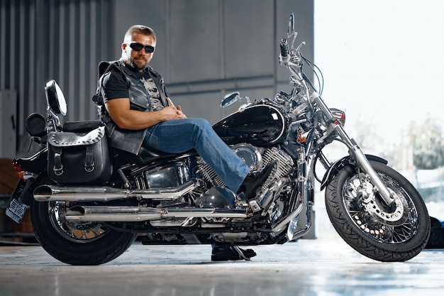 Bearded motorcyclist in black leather clothing with his motorbike on underground parking