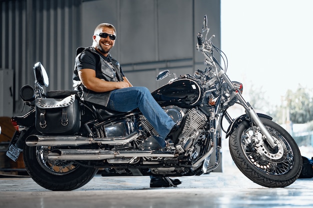 Bearded motorcyclist in black leather clothing with his motorbike