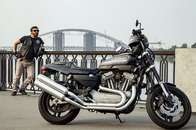 Bearded motorcyclist man with his motorbike on summertime posing.