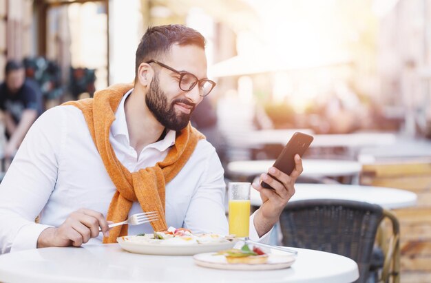Бородатый мультикультурный бизнесмен в белой рубашке разговаривает по телефону в кафе