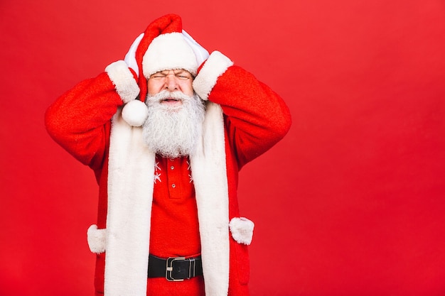 bearded old man in santa costume with a migrane isolated on red background