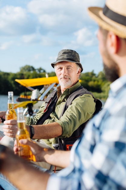 Фото Бородатый старик разговаривает с другом-мужчиной, попивая пиво и ловя рыбу