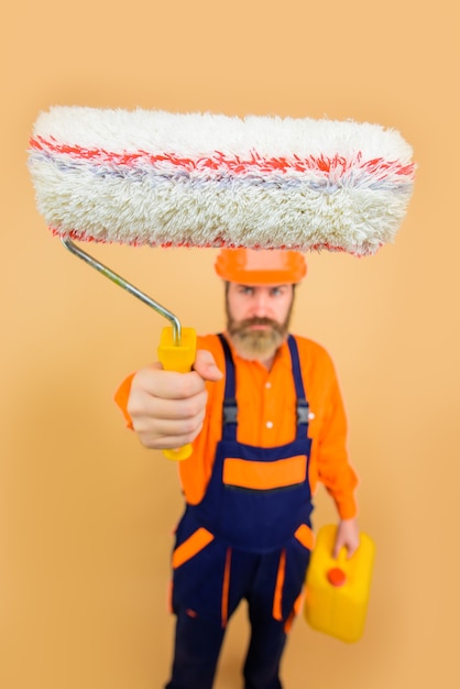 Bearded repairman in uniform holds paint roller repair man full height professional painter designer