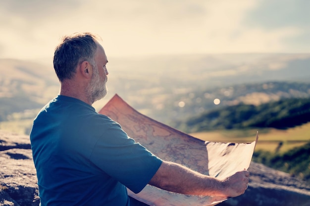 Il pensionato barbuto sta cercando una destinazione sulla mappa sullo sfondo dei campi