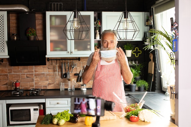 Bearded senior Man groenten voorbereiden om een bord eten beperkt door covid-19 thuis met masker te maken.