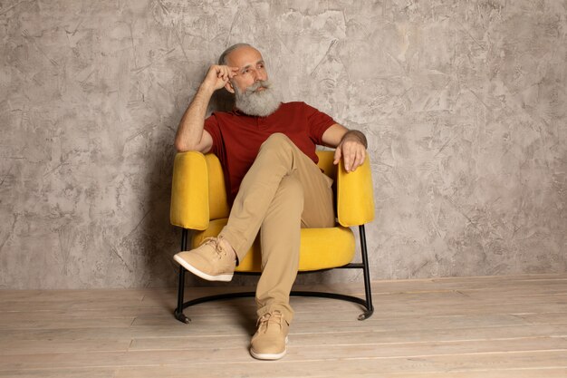 Bearded senior man relaxing in yellow armchair.