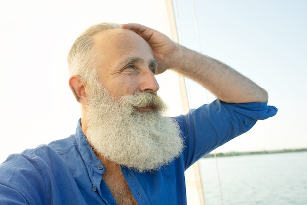 Uomo senior barbuto sulla barca a vela o sull'yacht che galleggia sul lago.