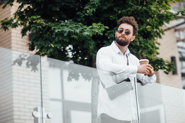 A bearded, serious, stylish manager on the streets of the city near modern office centre