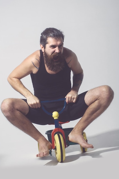 Bearded shouting happy man sitting on colorful bicycle toy