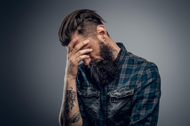 Bearded skinny man with tattooes feels dispair and sorrow while thinking about life.