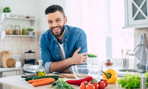 Uomo bello sorridente barbuto in cucina a casa è in posa e