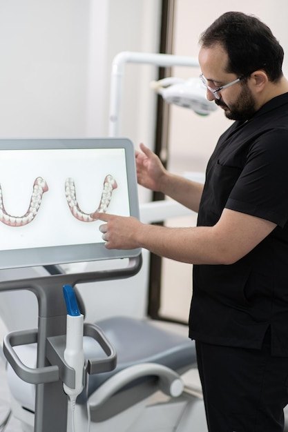 Bearded specialist in black uniform pointing to jaws models on computer screen using alternative