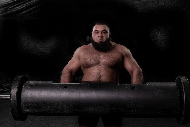 A bearded strong man holds a large iron log in his hands