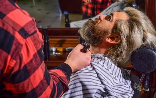 Bearded and stylish hipster man with beard cutting his hair in a barbershop Professional hairdressing work Lifestyle master barber does the hairstyle and styling with dryer Concept Barbershop