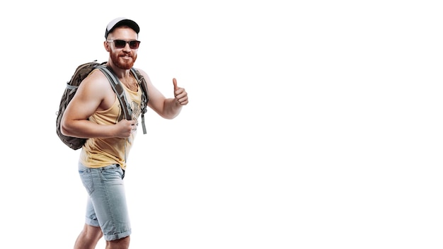 Bearded traveler man with backpack in a cap and sunglasses showing thumb up on white background