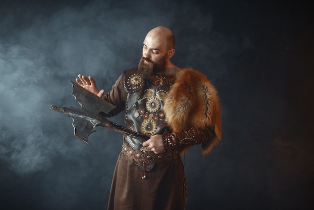 Bearded viking dressed in traditional nordic clothes touches the axe blade