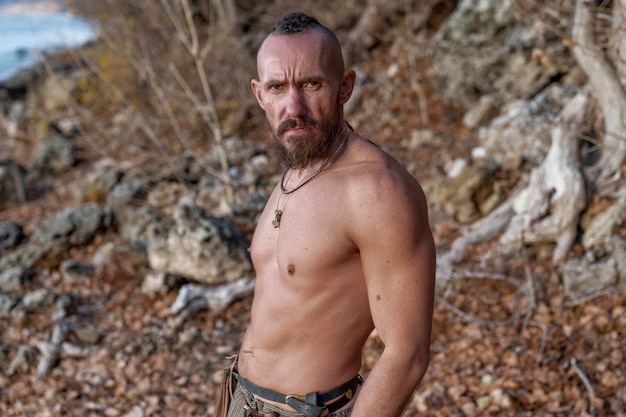 A bearded viking stands on the banks of the river among stones and trees