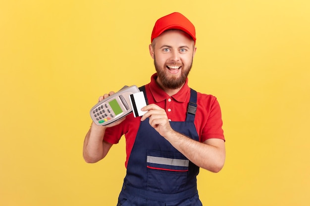 Бородатый рабочий мужчина держит pos-терминал для бесконтактной оплаты и кредитной карты для оплаты услуг