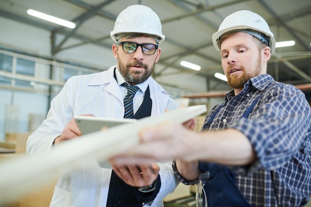 Bearded worker showing wooden plank to inspector