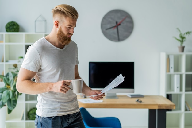 Bearded young businessman working at modern office.Man wearing white t-shirt and making notes on the documents.