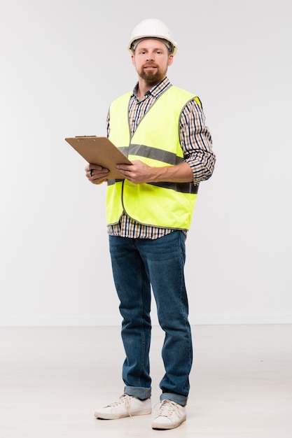 Bearded young engineer with clipboard standing in front of camera in isolation and looking at you