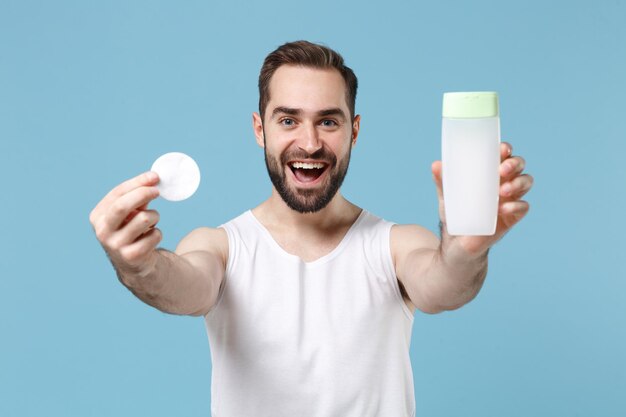 Bearded young man 20s years old in white shirt hold in hand\
cotton pad isolated on blue pastel wall background, studio\
portrait. skin care healthcare cosmetic procedures concept. mock up\
copy space.