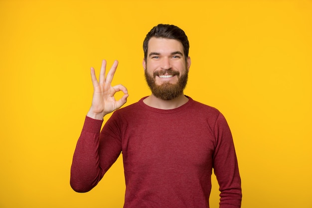 Bearded young man is showing OK gesture  on yellow background.