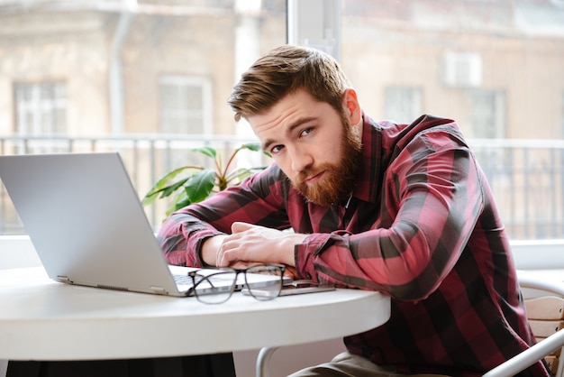 Бородатый молодой человек, сидя в кафе при использовании портативного компьютера.