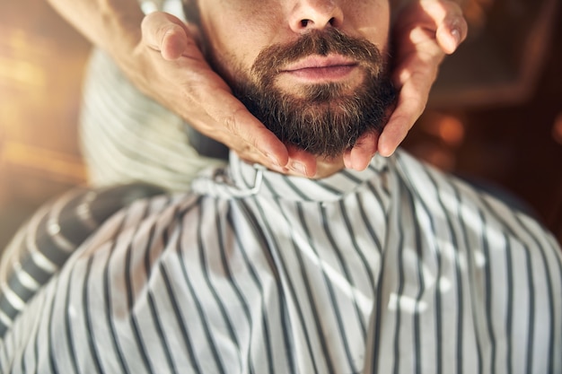 写真 ヘアスタイリストが彼のひげに触れている間、理髪店の予定で笑っているひげを生やした若い男