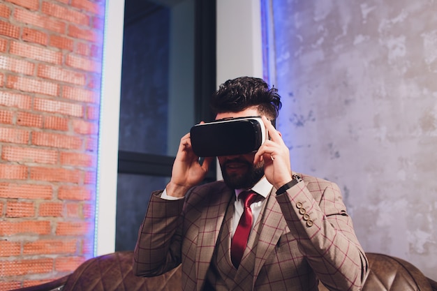 Изумлённые взгляды виртуальной реальности бородатого молодого человека нося в современной coworking студии.