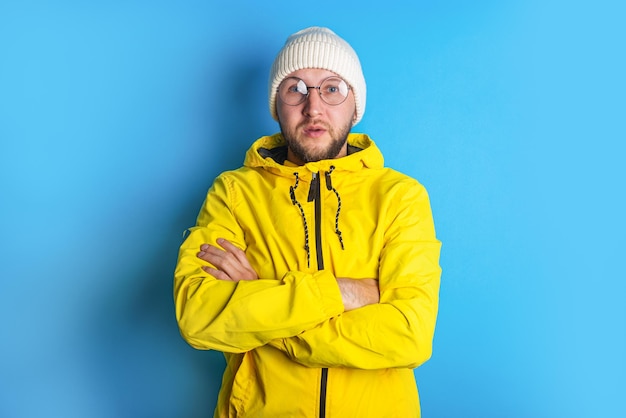 Bearded young man with glasses in a yellow jacket on a blue background