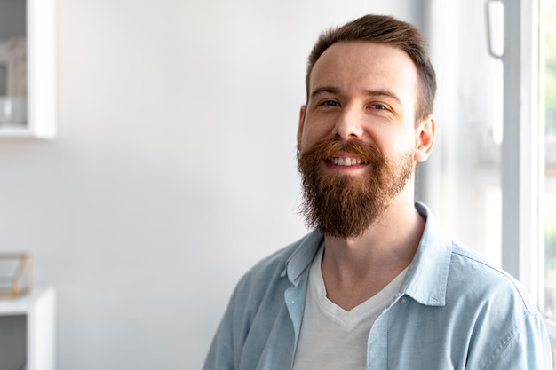 Beardige, glimlachende, knappe jonge man die alleen thuis staat.