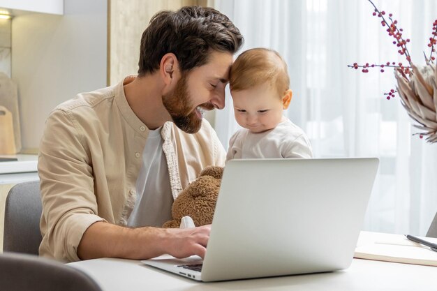Beardige jonge blanke man die thuis werkt terwijl hij voor zijn kleine zoon zorgt