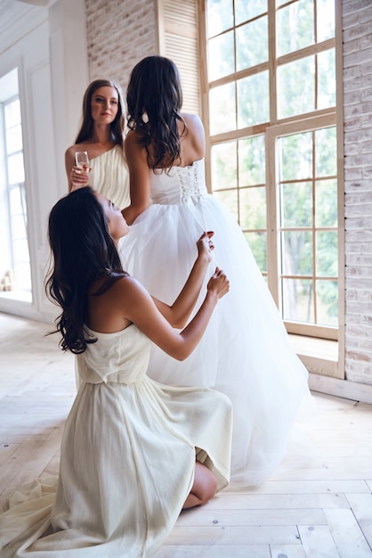 ビートの友達はいつも周りにいます。試着室で美しい花嫁を助けながらウェディングドレスのコルセットを結ぶ花嫁介添人の全長